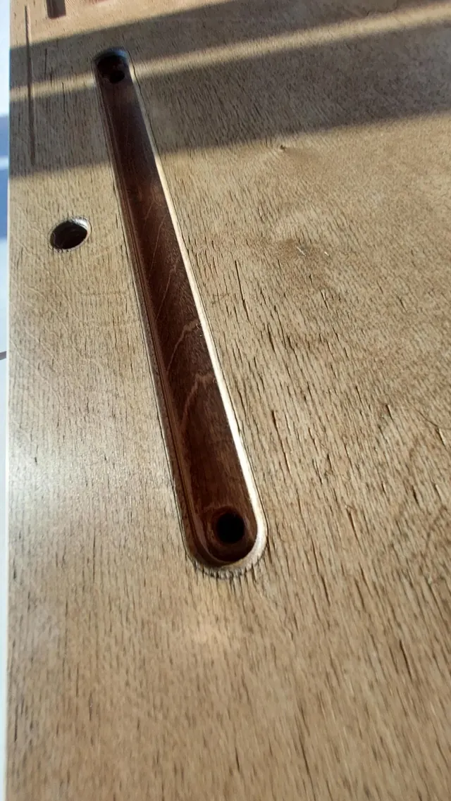 Close detail of the routed ash groove — a long, rounded channel with a socket at one end — cut into pale birch, the grain visible around it.