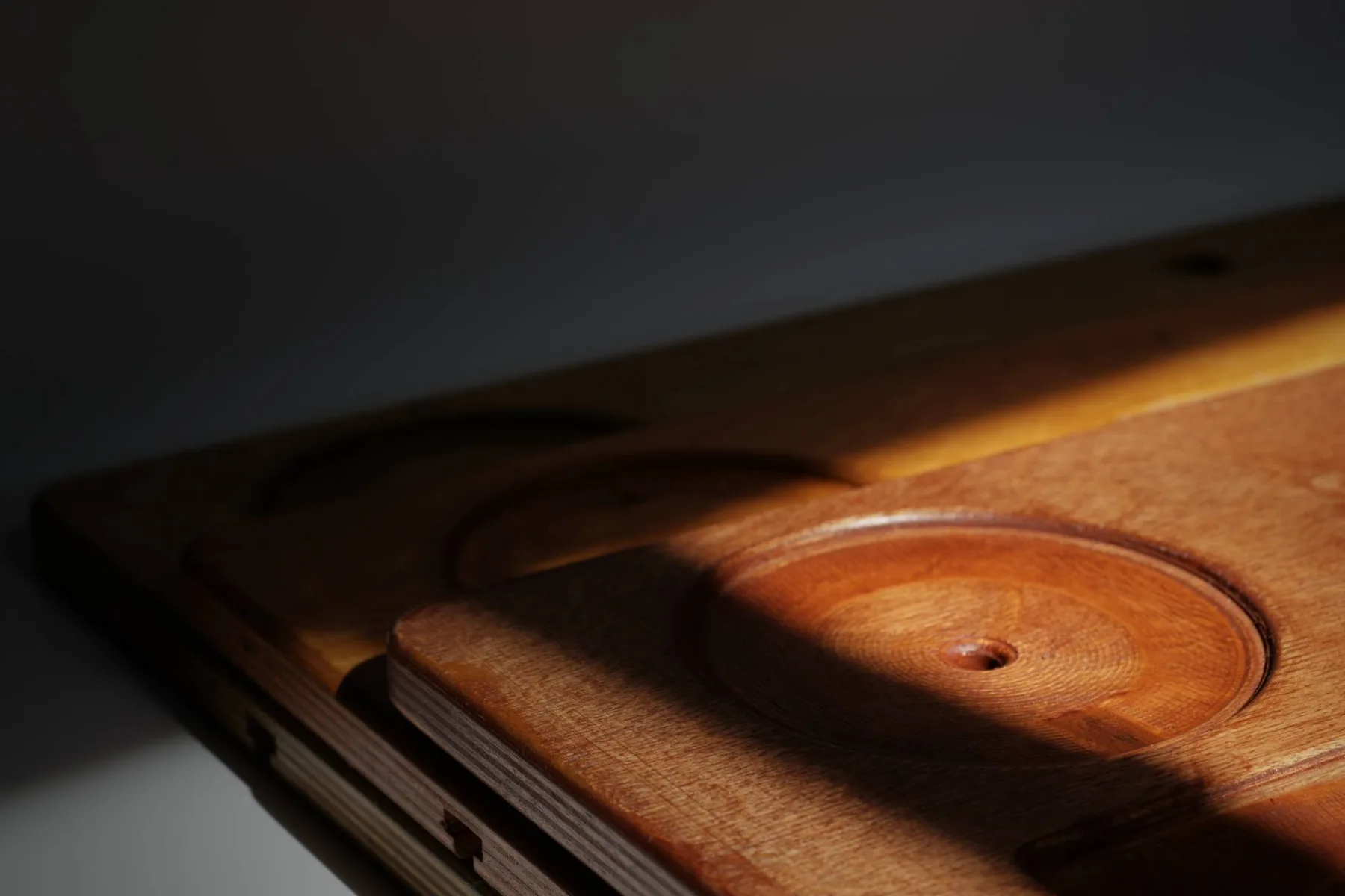 Close-up of a finished board's corner in raking light: the recessed candle holder with its centre pin, and the cross-ply birch layers visible along the edge.