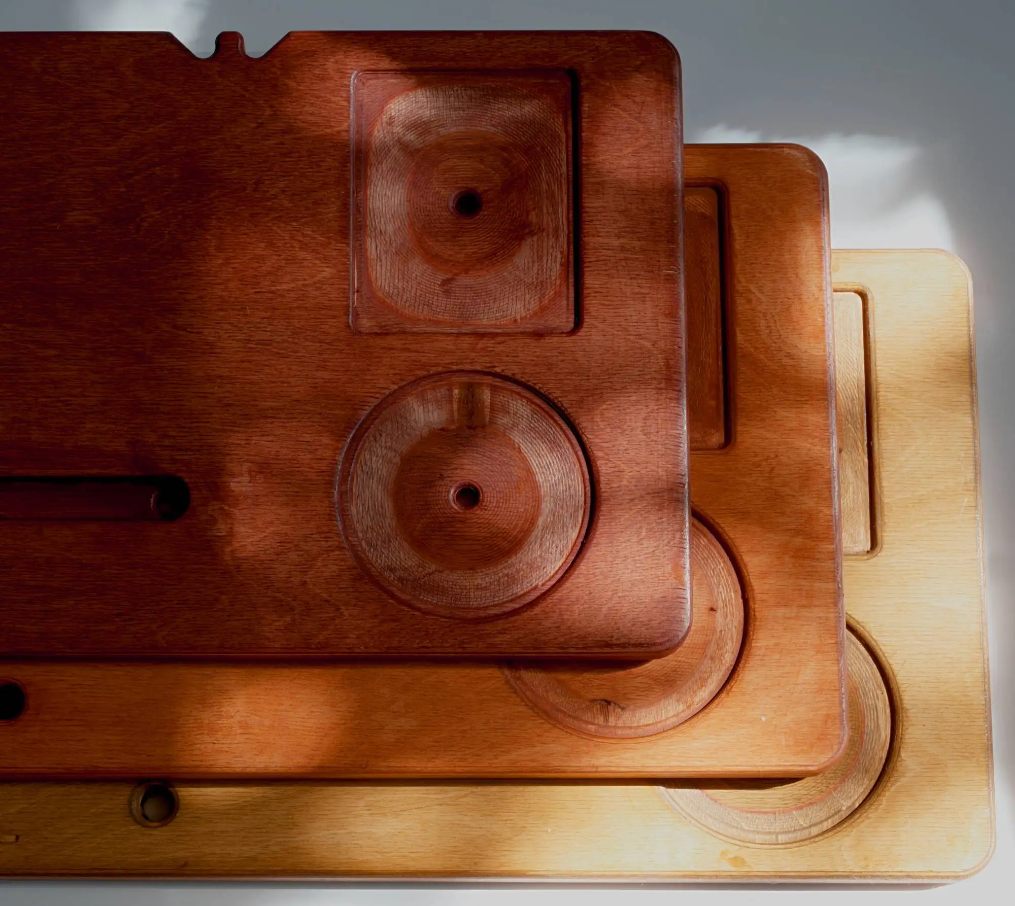 Three bath boards stacked and overlapping, in three finishes from dark stain to pale raw birch, showing the recessed cup well, soap tray, and book slot.