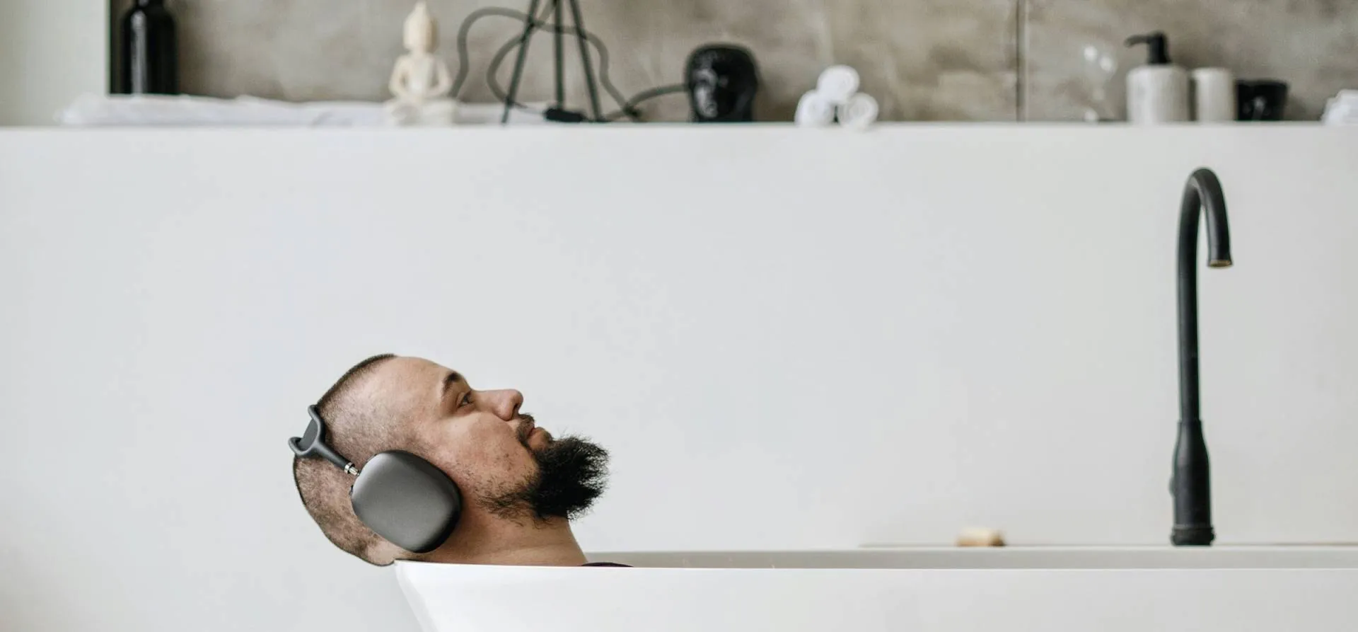 A person lying back in a bath wearing large over-ear headphones