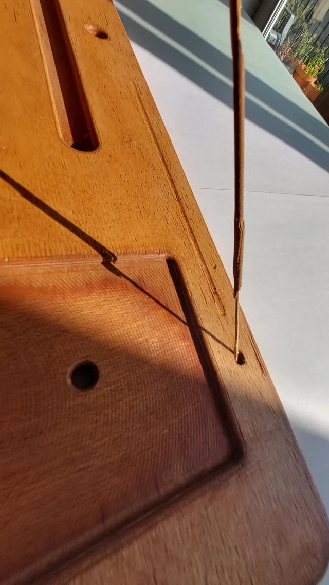 A stick of incense standing upright in the board’s incense socket, its shadow thrown across the surface in low afternoon light.
