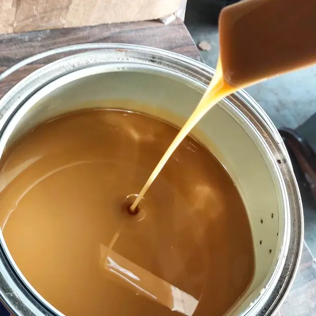 Warm amber stain running off a stir stick back into an open tin in the workshop.