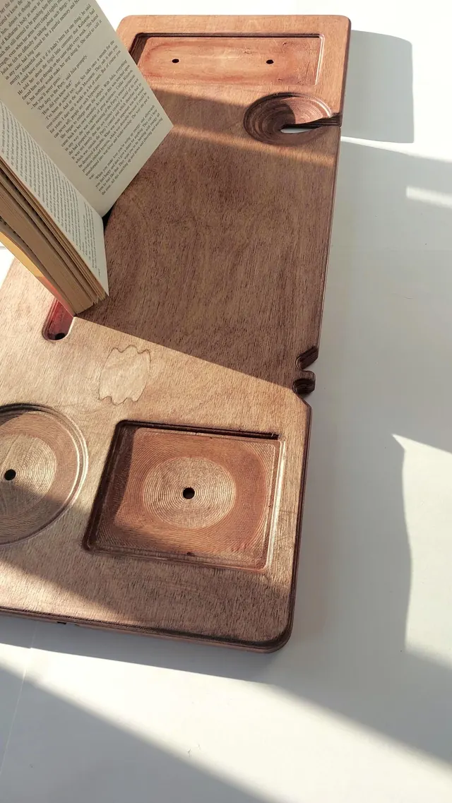 An open book resting across a warm brown board, the recessed soap and candle trays beside it in raking sunlight.