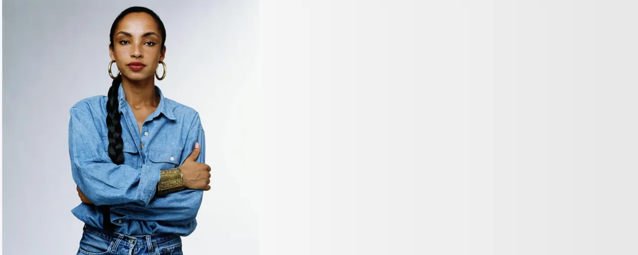 A woman in a denim shirt leaning against a plain white wall